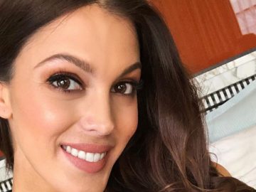 Iris Mittenaere en robe décolletée blanche et argenté sur le tapis rouge rangeant une mèche de cheveux