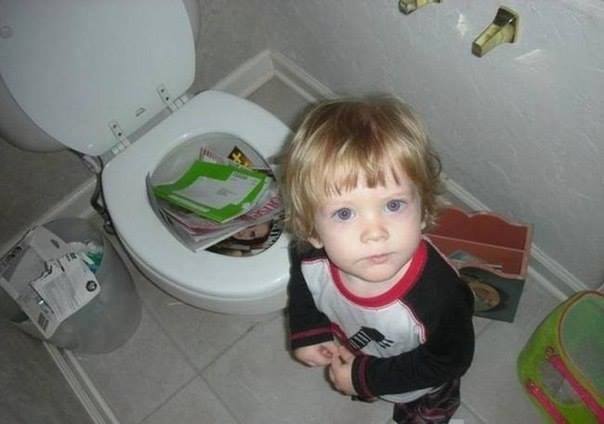 Un enfant met des livres dans la cuvette des WC