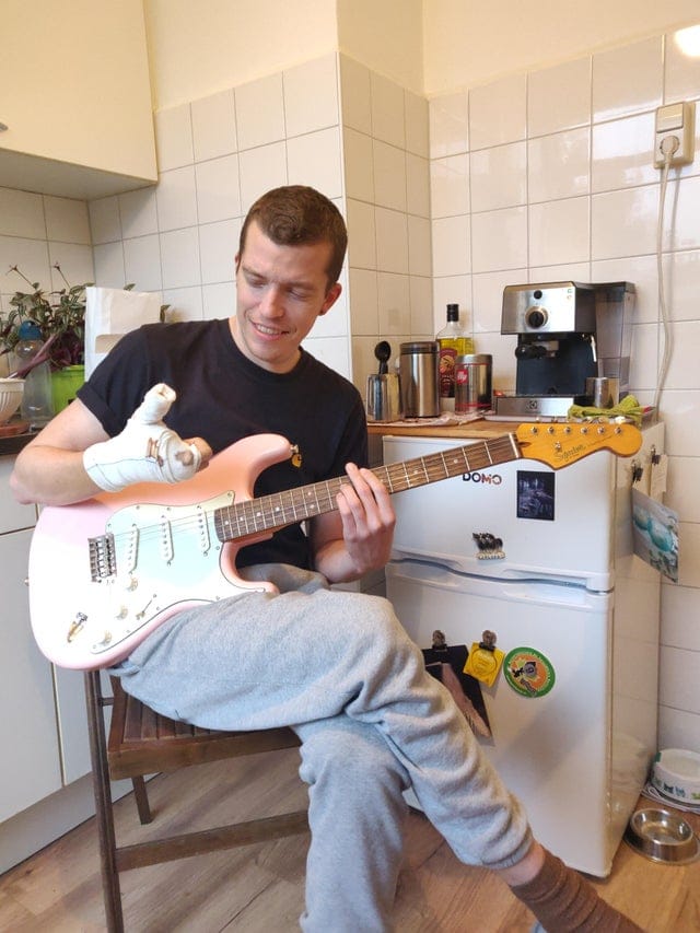 Il tient sa nouvelle guitare électrique avec son plâtre et ses deux doigts en moins