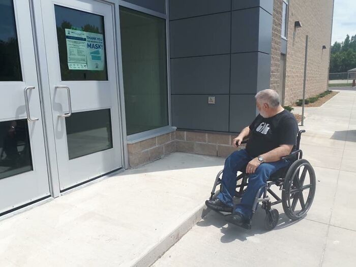 Une personne en chaise roulante à l'entrée d'un immeuble.